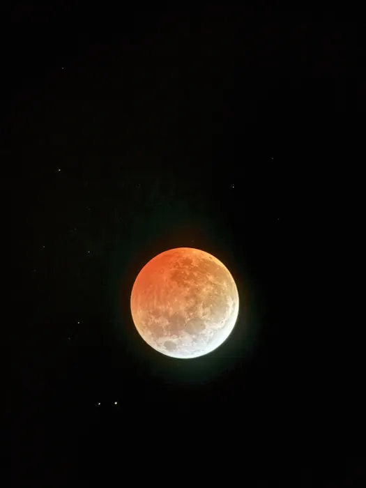 One of many images from the lunar eclipse in March of 2025. This depicts the moon with the upper three quarters tinted orange by a lunar eclipse and the bottom crescent white.